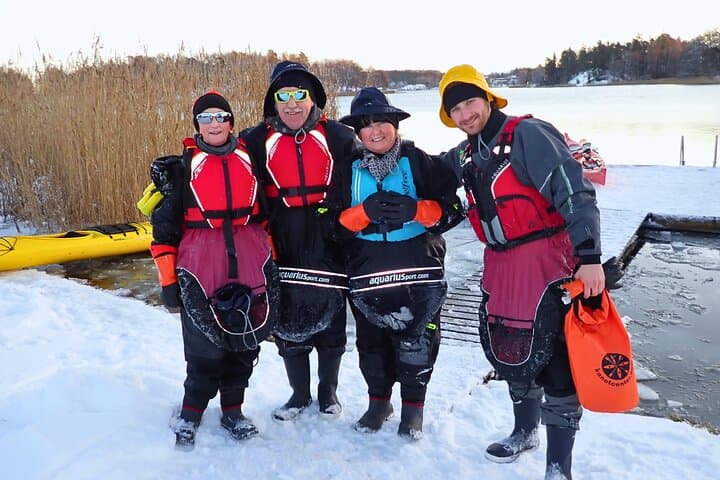 Excited paddlers preparing for a guided winter kayaking experience near Vaxholm, dressed in warm drysuits for comfort and safety